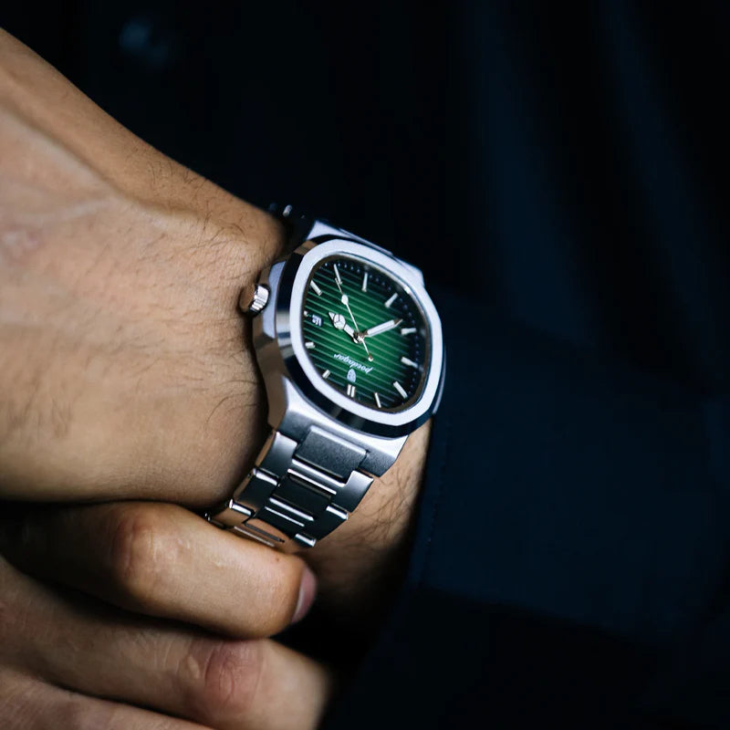 Close-up of a hand wearing a silver watch with a green face against a dark background